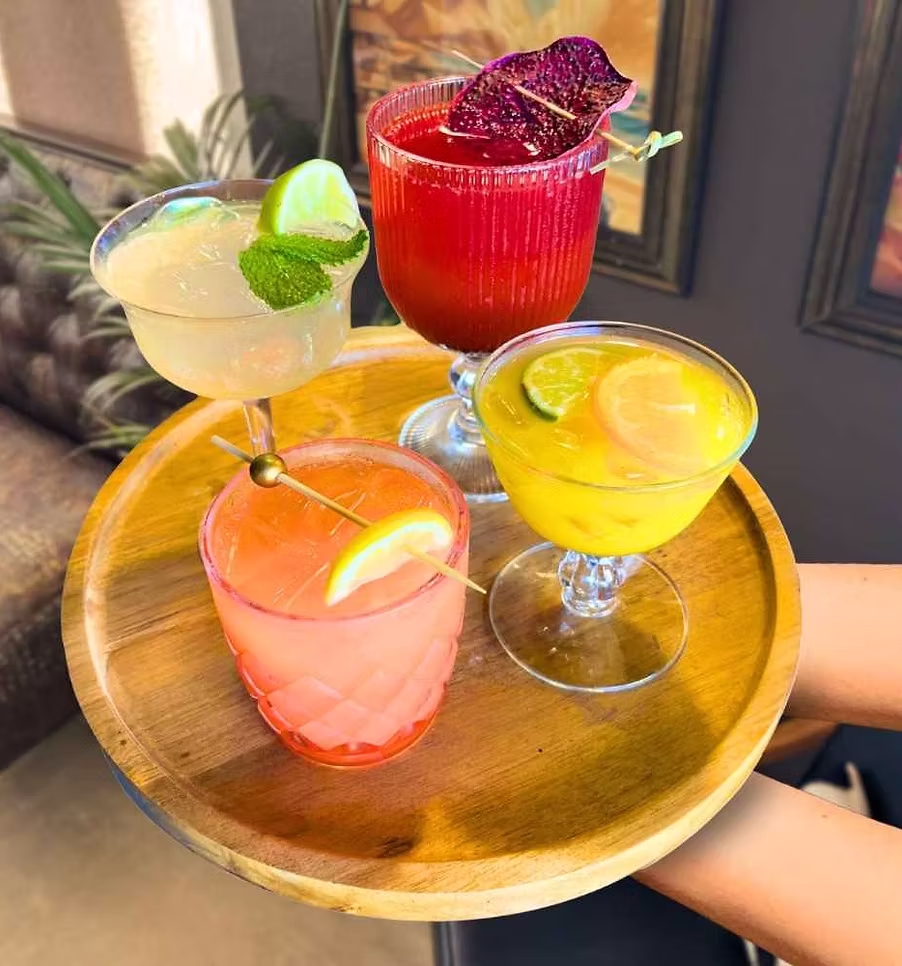 4 mocktails of various colors on a tray held by a server