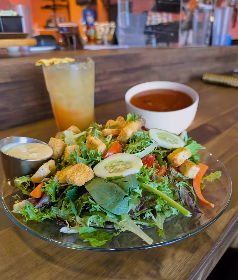 a salad and soup are positioned on the table with a drink nearby